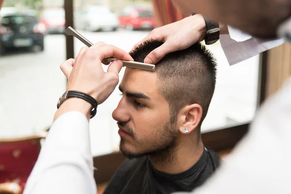 Парикмахер бреет лоб натуральной бритвой — стоковое фото