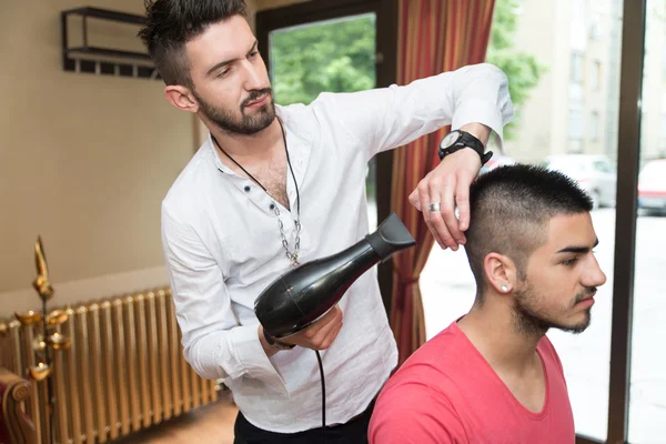 Friseur föhnt Mann im Geschäft die Haare ab — Stockfoto