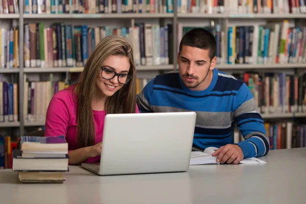 Estudiantes felices trabajando con computadora portátil en la biblioteca —  Fotos de Stock
