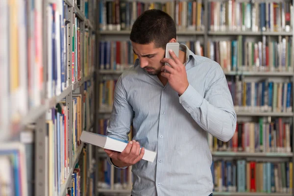 Hermoso estudiante universitario usando el teléfono móvil en la biblioteca —  Fotos de Stock