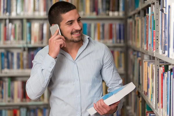 Estudante masculino conversando ao telefone na biblioteca — Fotografia de Stock