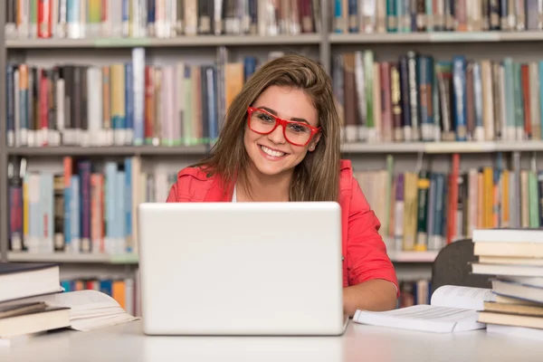 Mutlu kız öğrenci dizüstü bilgisayar kitaplığı ile çalışma — Stok fotoğraf