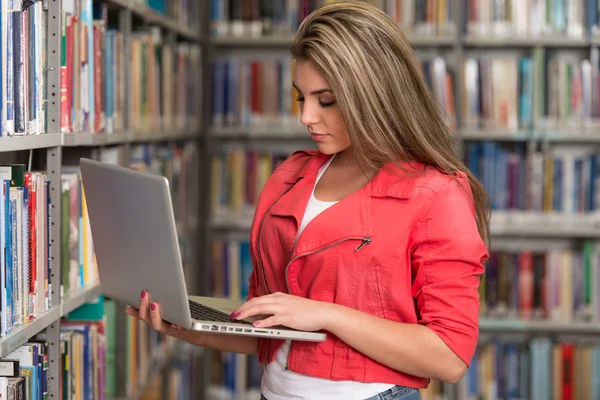 Счастливая студентка с ноутбуком в библиотеке — стоковое фото