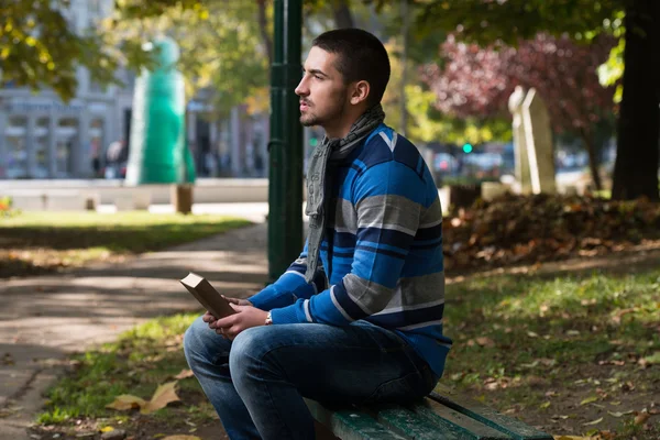 Knappe jongeman die een boek leest in het park — Stockfoto