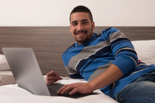 Dizüstü bilgisayar kullanarak yatakta gülümseyen genç öğrenci — Stok fotoğraf