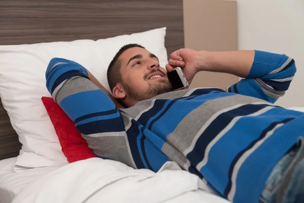 Felice giovane uomo utilizzando il telefono sul letto — Foto Stock