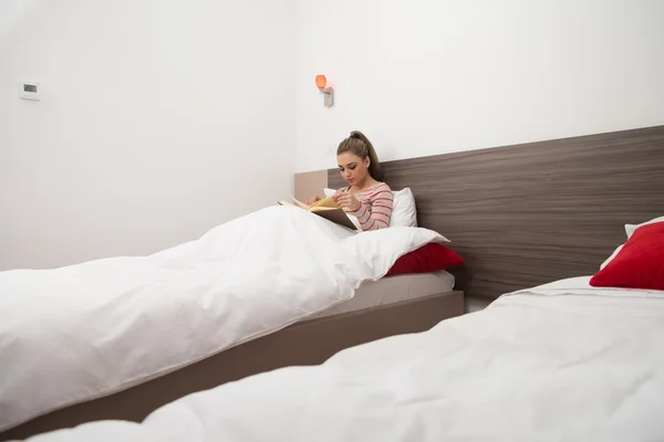 Šťastná mladá žena čtení knihy na postel — Stock fotografie