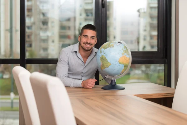 Bonito jovem segurando um globo no escritório — Fotografia de Stock