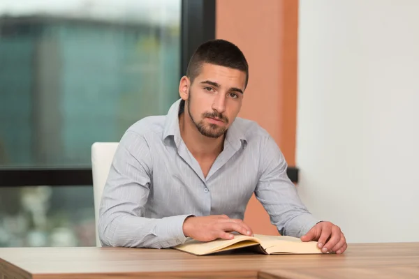 Glücklicher Student in der Bibliothek, der ein Buch liest — Stockfoto