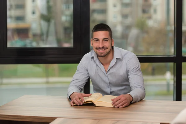 Lächelnder junger Student in Bibliothek liest Buch — Stockfoto