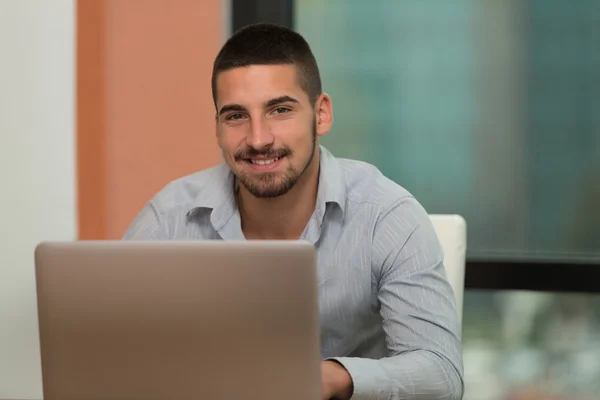 Lächelnder junger Student in der Bibliothek mit seinem Laptop — Stockfoto