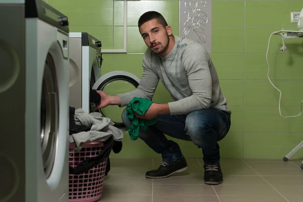 Jeune homme mettant un tissu dans la machine à laver — Photo