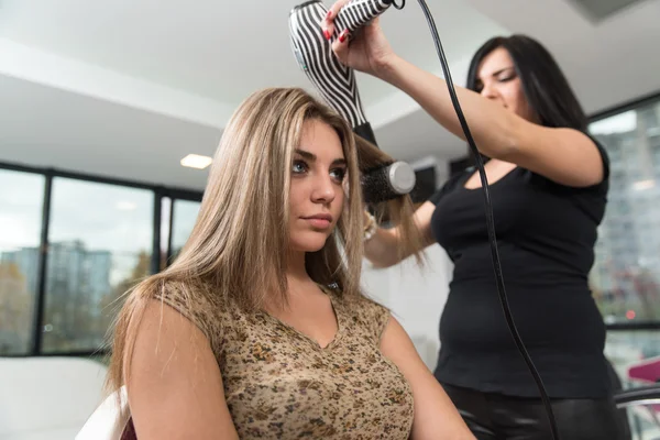 Στυλίστας μαλλιά χρησιμοποιώντας το στεγνωτήριο σε γυναίκα στο σαλόνι — Φωτογραφία Αρχείου