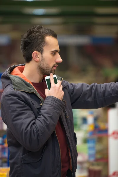 Człowiek przy użyciu telefonu komórkowego podczas robienia zakupów w supermarkecie — Zdjęcie stockowe