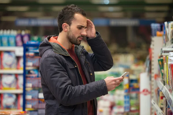 Człowiek przy użyciu telefonu komórkowego podczas robienia zakupów w supermarkecie — Zdjęcie stockowe