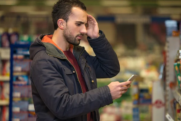 Uomo che sembra confuso al telefono cellulare nel supermercato — Foto Stock