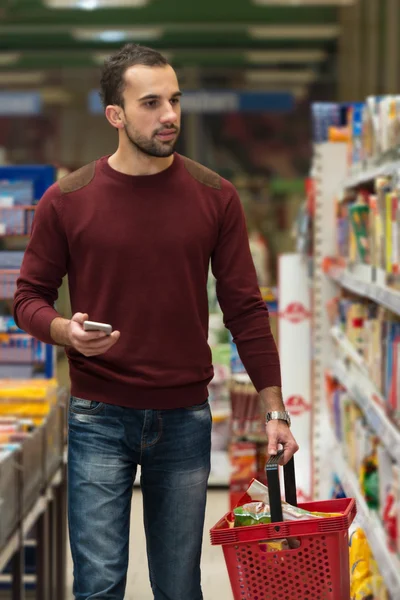 Młody człowiek wpisując na telefon komórkowy w supermarkecie — Zdjęcie stockowe