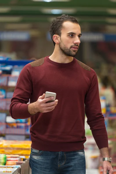 Mann benutzt Handy beim Einkaufen im Supermarkt — Stockfoto