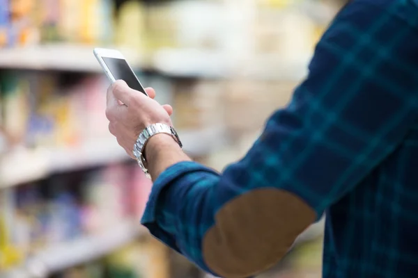 Mand ved hjælp af mobiltelefon, mens shopping i supermarkedet - Stock-foto