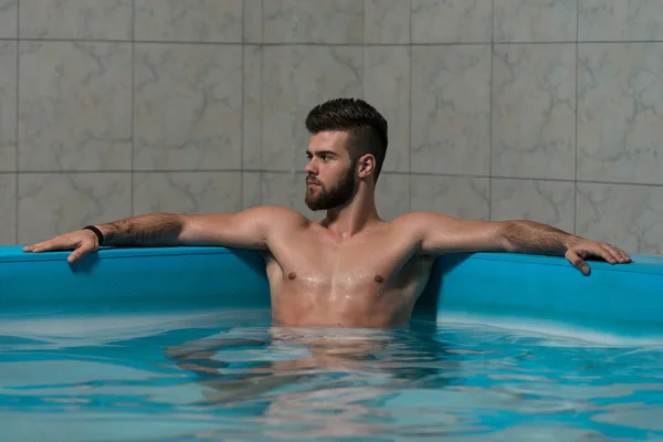 Homem descansando relaxado na borda da piscina — Fotografia de Stock