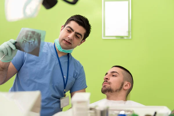 Zahnarzt hält Röntgenbild und untersucht weißen Patienten — Stockfoto