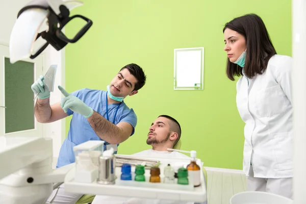 Zahnarzt hält Röntgenbild und untersucht weißen Patienten — Stockfoto