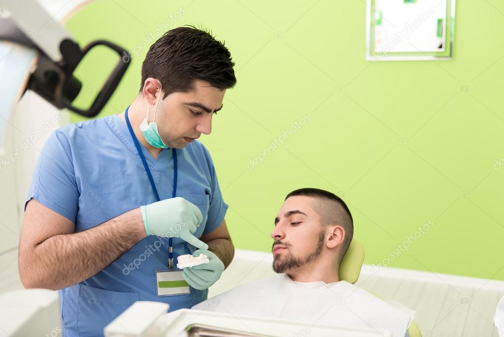 Dentist Explaining Artificial Teeth To Patient In Clinic