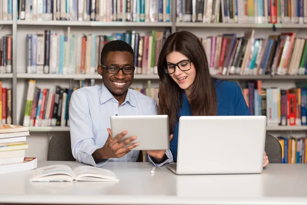 Estudantes felizes trabalhando com laptop na biblioteca — Fotografia de Stock