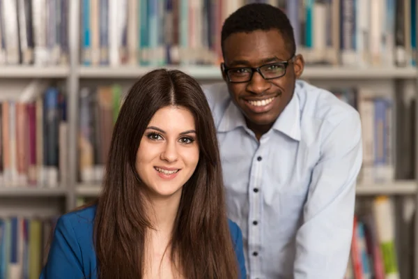 Šťastní studenti pracující s přenosným počítačem v knihovně — Stock fotografie