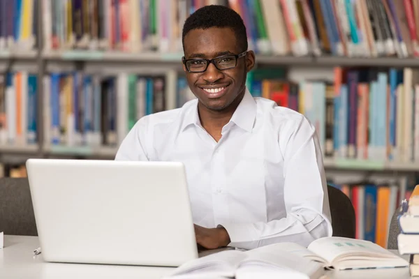 Felice africano maschio studente con computer portatile in biblioteca — Foto Stock
