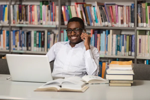 Hermoso estudiante universitario usando el teléfono móvil en la biblioteca — Foto de Stock