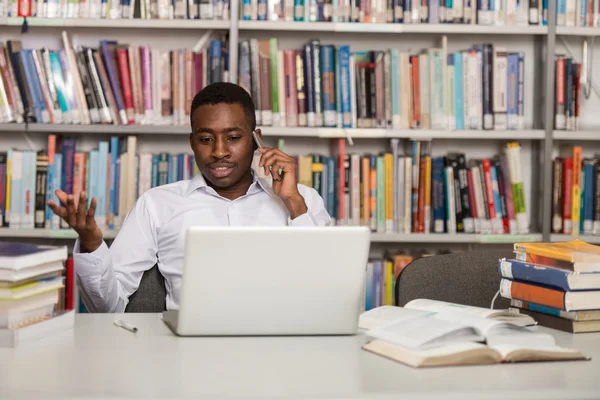 Przystojnego studenta przy użyciu telefonu komórkowego w bibliotece — Zdjęcie stockowe