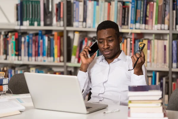 Estudante universitário bonito usando telefone celular na biblioteca — Fotografia de Stock