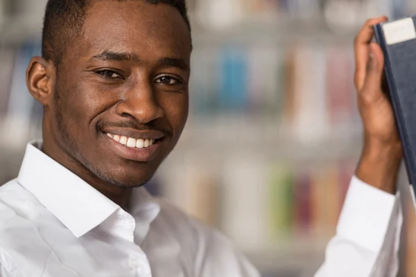 Bonito jovem estudante universitário em uma biblioteca — Fotografia de Stock