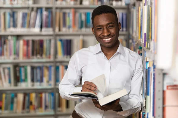 Bonito jovem estudante universitário em uma biblioteca — Fotografia de Stock