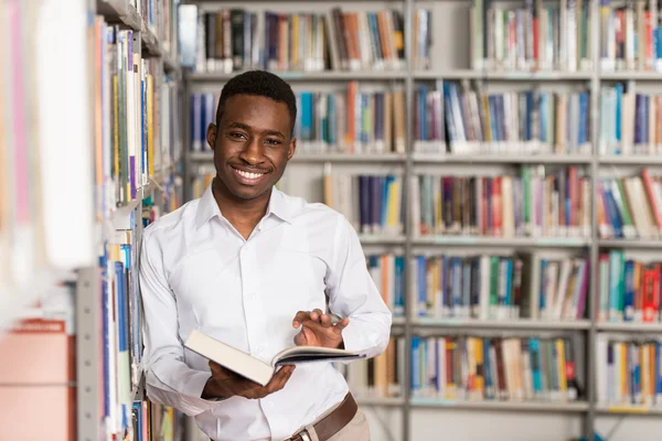 Estudante masculino feliz com livro na biblioteca — Fotografia de Stock