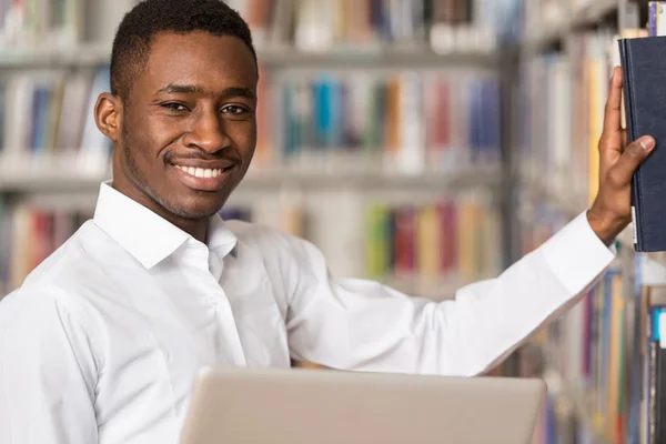 Estudante masculino feliz trabalhando com laptop na biblioteca — Fotografia de Stock