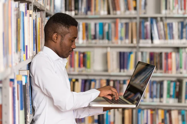 Estudante masculino feliz trabalhando com laptop na biblioteca — Fotografia de Stock