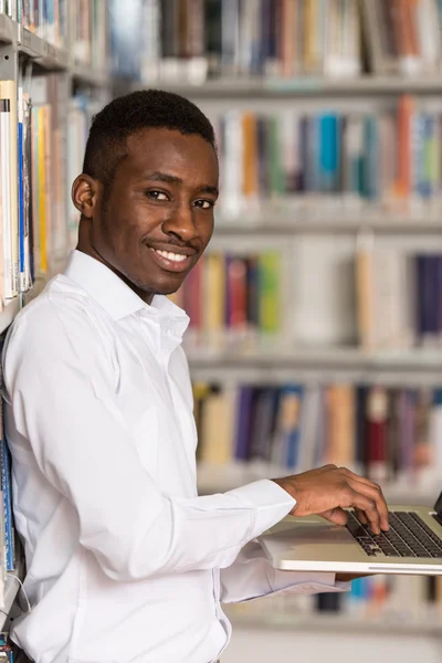 Feliz estudiante masculino con ordenador portátil en la biblioteca — Foto de Stock
