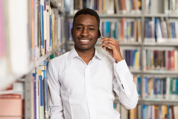 Étudiant beau collège utilisant le téléphone portable dans la bibliothèque — Photo