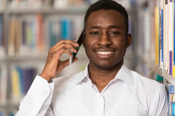 Estudante masculino conversando ao telefone na biblioteca — Fotografia de Stock