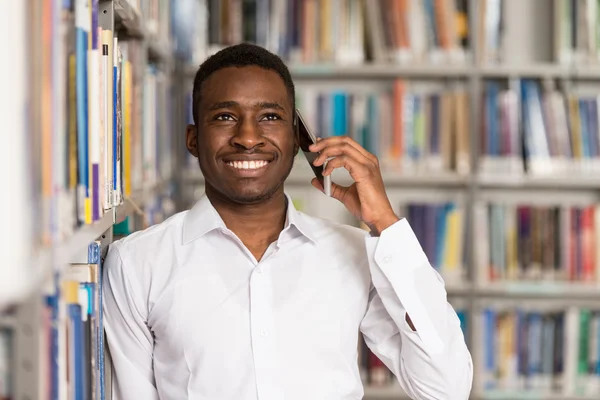 Hermoso estudiante universitario usando el teléfono móvil en la biblioteca — Foto de Stock