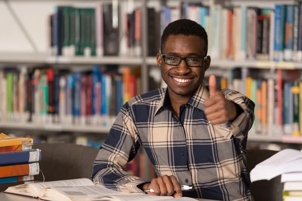 Africain dans une bibliothèque montrant pouces vers le haut — Photo