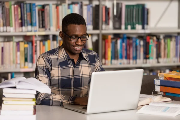 Jeune étudiant utilisant son ordinateur portable dans une bibliothèque — Photo