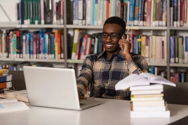 Stilig collegestudent med mobiltelefon i biblioteket — Stockfoto