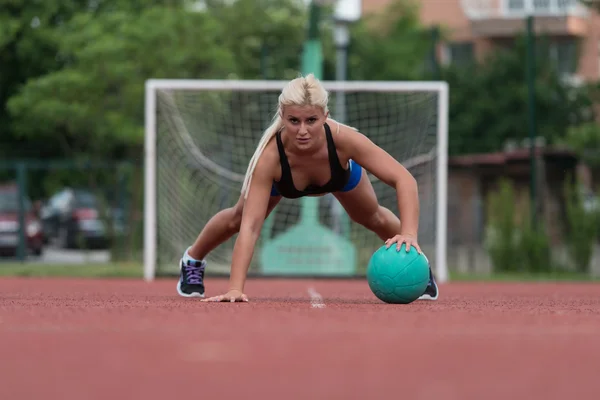 Mujer joven haciendo ejercicio push-ups en la bola de la medicina al aire libre — Foto de Stock