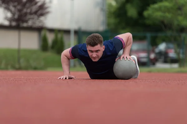 Hombre joven haciendo ejercicio push-ups en la bola de la medicina al aire libre — Foto de Stock