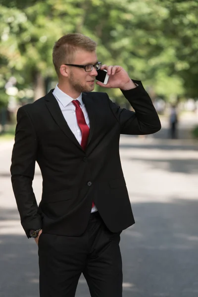 Uomo d'affari a piedi all'aperto nel parco durante l'utilizzo di telefono cellulare — Foto Stock
