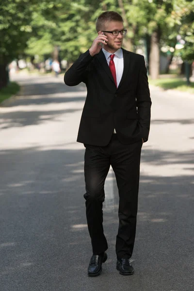 Affärsman promenader ute i parken medan du använder mobiltelefon — Stockfoto