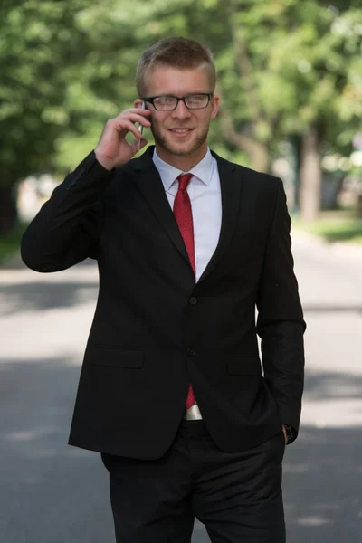 Homme d'affaires marchant à l'extérieur dans le parc tout en utilisant le téléphone mobile — Photo